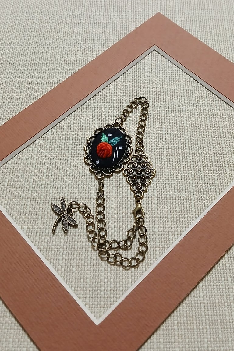 Decorative bronze chain bracelet with ornate red and black floral pendant and star charm on white mat with tan frame