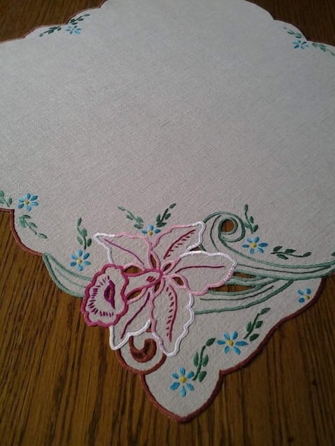 Embroidered white handkerchief with pink iris flower and blue floral details on wooden surface