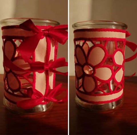 Two glass candle holders with red decorative wraps and bows tied around them, displayed side by side.