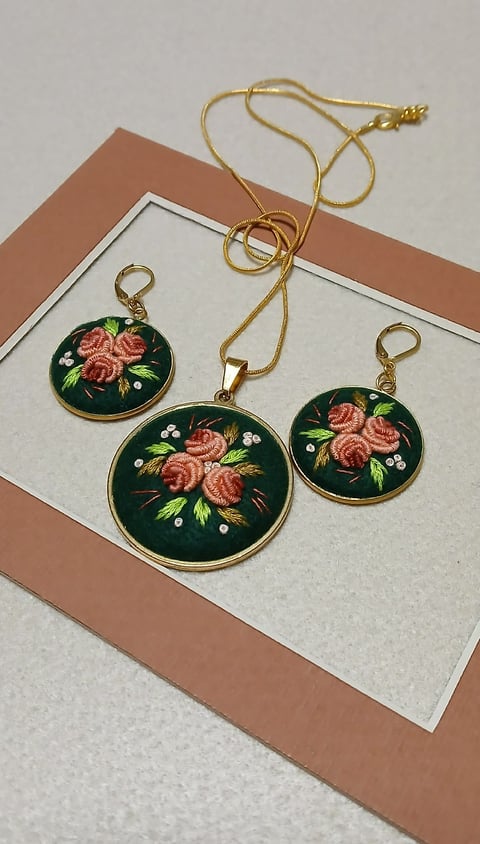 Three gold-framed enamel pendant charms with floral rose designs on dark green background, displayed with a gold chain