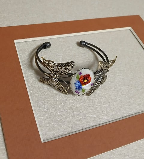 Ornate silver bracelet with filigree butterfly wings and floral porcelain centerpiece featuring red and blue flowers