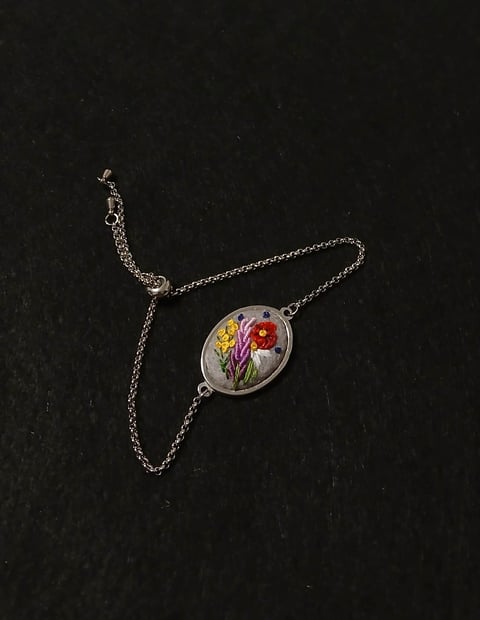 Silver chain necklace with oval pendant containing pressed yellow and red flowers on dark background