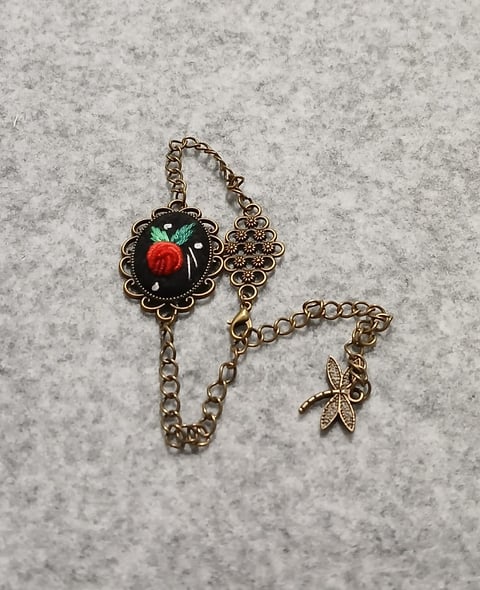 Vintage-style brass charm bracelet with red rose cameo centerpiece and starfish pendant on concrete background