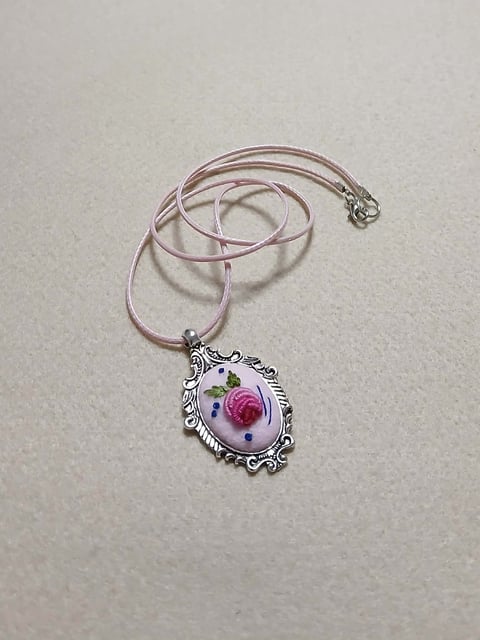 Pink cord necklace with ornate silver oval pendant featuring pressed pink flower and green leaf design