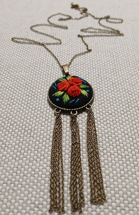 Vintage-style pendant necklace with red roses on black enamel, three dangling chain tassels, and bronze chain.