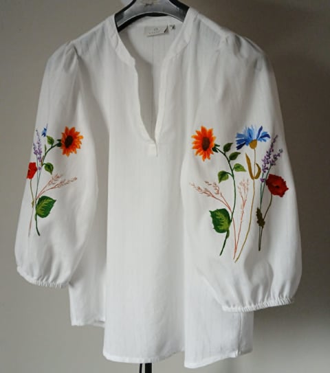 White blouse with colorful embroidered flowers on front, displayed on a hanger