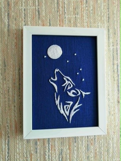 Framed artwork of a white wolf silhouette howling at the moon with stars on a dark blue background