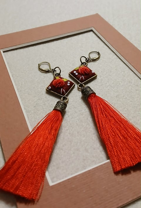 Pair of handmade earrings with deep red tassels and burgundy square resin tops displayed on white card in tan frame