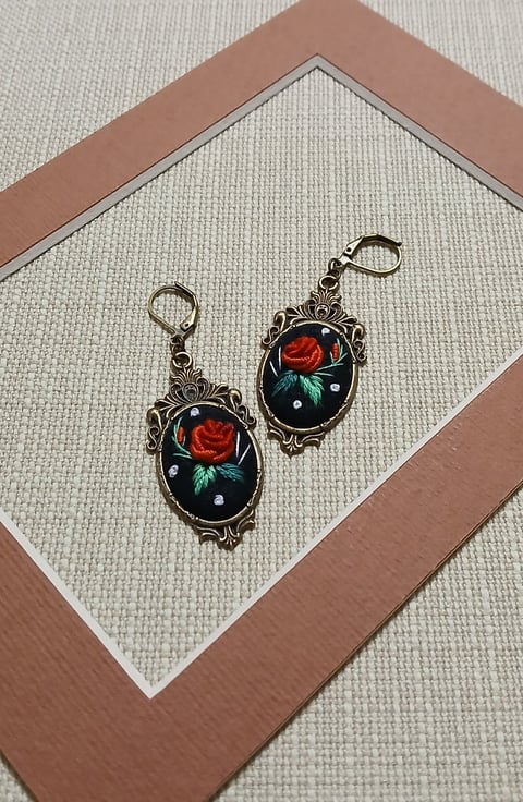 Pair of ornate metal charm earrings with red rose and blue flower designs on black enamel background