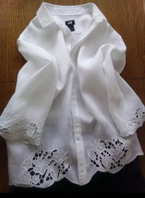 White H&M button-up shirt with lace trim detailing on the sleeves, laid out on a wooden floor