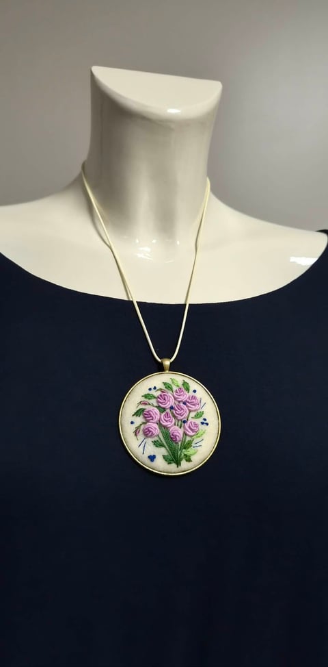 Embroidered floral pendant necklace with purple roses on cream background, displayed on a mannequin wearing a dark blue top.