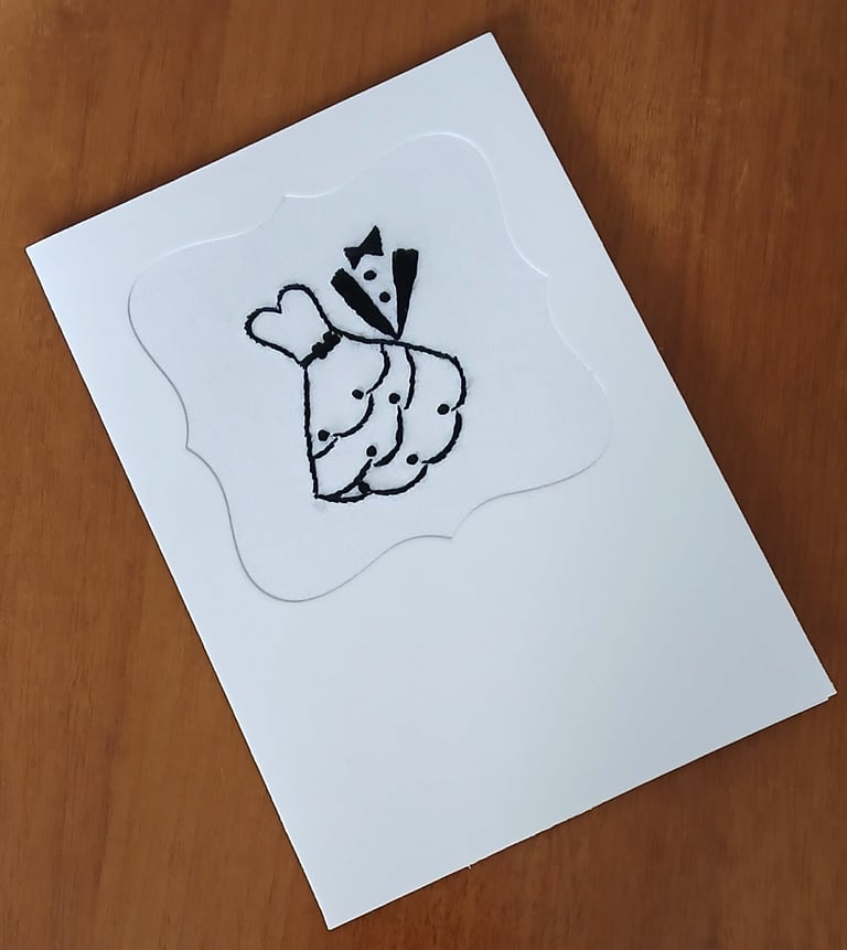 Handwritten sketch on white card showing two mitten hands holding a heart with a party hat, on wooden surface