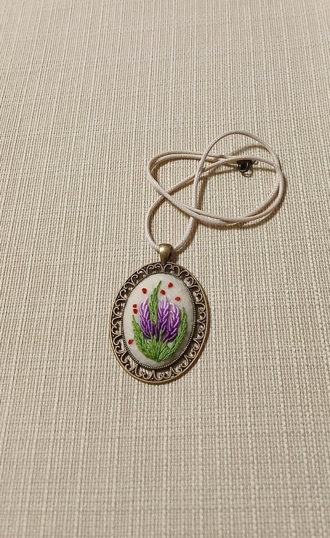 Ornate silver pendant necklace with purple lavender flowers and pink beads on white background