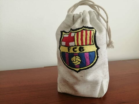 Small cream-colored cloth drawstring pouch featuring an embroidered FC Barcelona crest on wooden surface