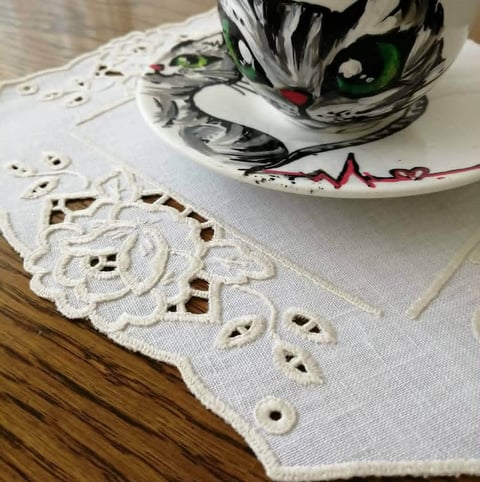 White linen napkins with embroidered floral cutout details displayed on a wooden table with a decorative ceramic bowl