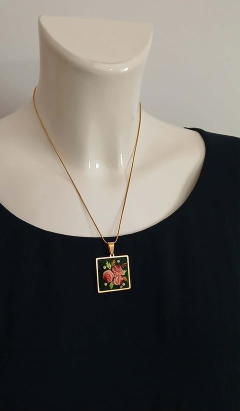 Gold chain necklace with square pendant featuring red floral design on black background, displayed on white mannequin bust
