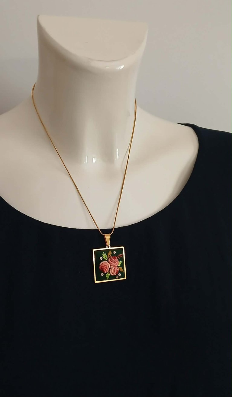 Gold chain necklace with square pendant featuring red floral design on black background, displayed on white mannequin bust