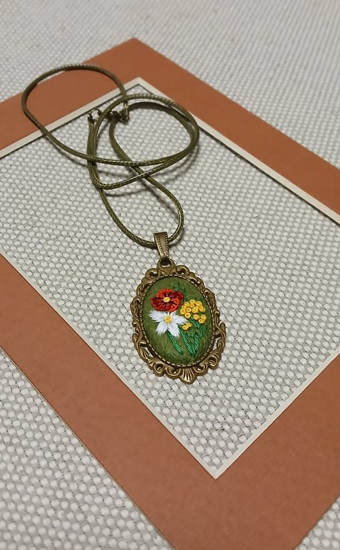 Vintage brass oval pendant necklace with embroidered flowers on tan and beige striped background