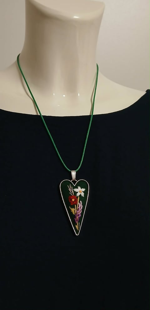 Heart-shaped pendant necklace with colorful pressed flowers on green cord, displayed on a mannequin wearing a black top