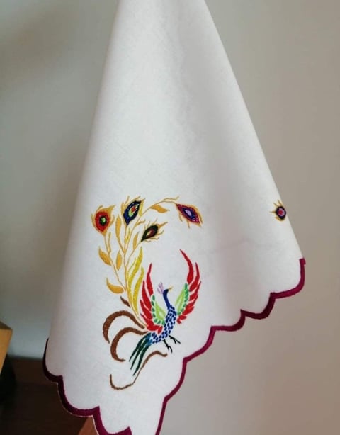White fabric with colorful embroidered peacock and floral design, bordered with burgundy scalloped trim