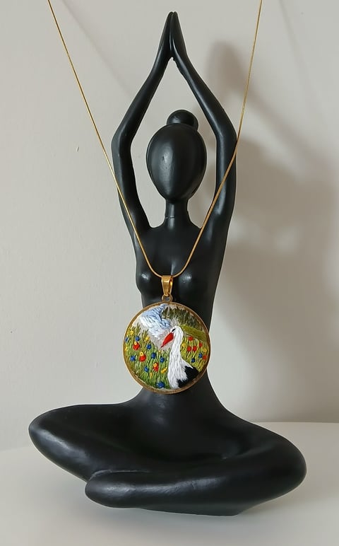 Black meditation yoga figurine with arms raised holding a pendant necklace featuring a colorful landscape painting