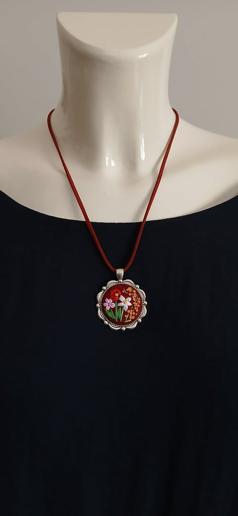 Mannequin wearing red string necklace with ornate circular pendant featuring red enamel and white floral design