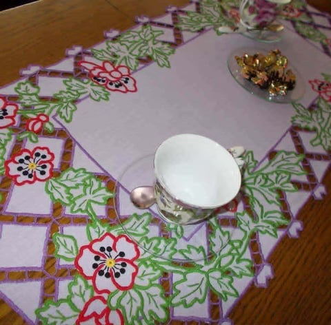 White teacup with saucer on a decorative floral purple tablecloth with red and green flower patterns