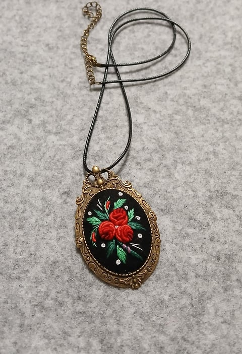 Ornate gold pendant necklace with black enamel face decorated with red roses and green leaves on black cord