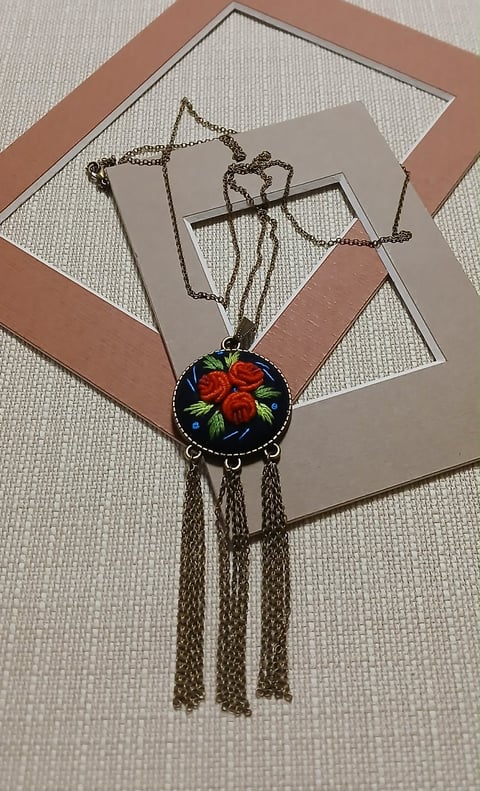 Hand-painted enamel pendant necklace featuring red roses on dark background, with triple chain tassels, displayed on decorative cardboard frames