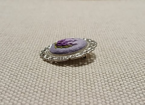 Silver ornate brooch with purple oval stone cabochon on textured fabric background