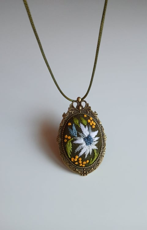 Antique brass oval pendant necklace with embroidered white daisy and yellow floral design on olive cord
