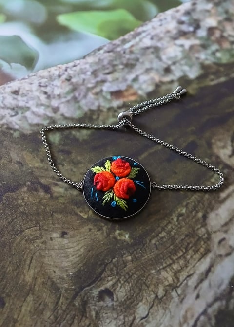 Pendant necklace with red roses design on black background, lying on textured tree bark