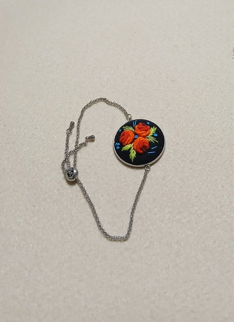 Silver chain necklace with circular pendant featuring red roses on dark background