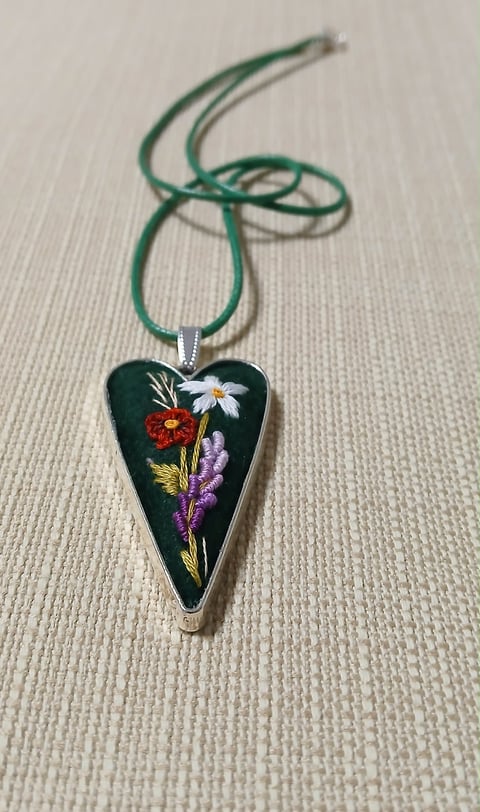 Heart-shaped pendant with pressed flowers on a dark resin background, suspended from a green cord necklace