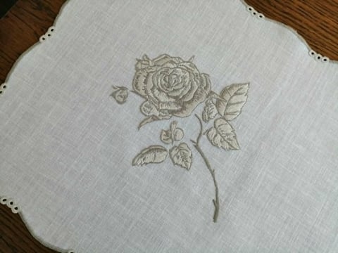 Embroidered rose with stem and leaves on white linen fabric placed on wooden surface