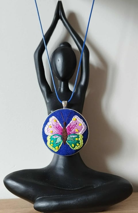 Black abstract statue wearing blue cord necklace with embroidered butterfly pendant in purple, yellow, and green colors