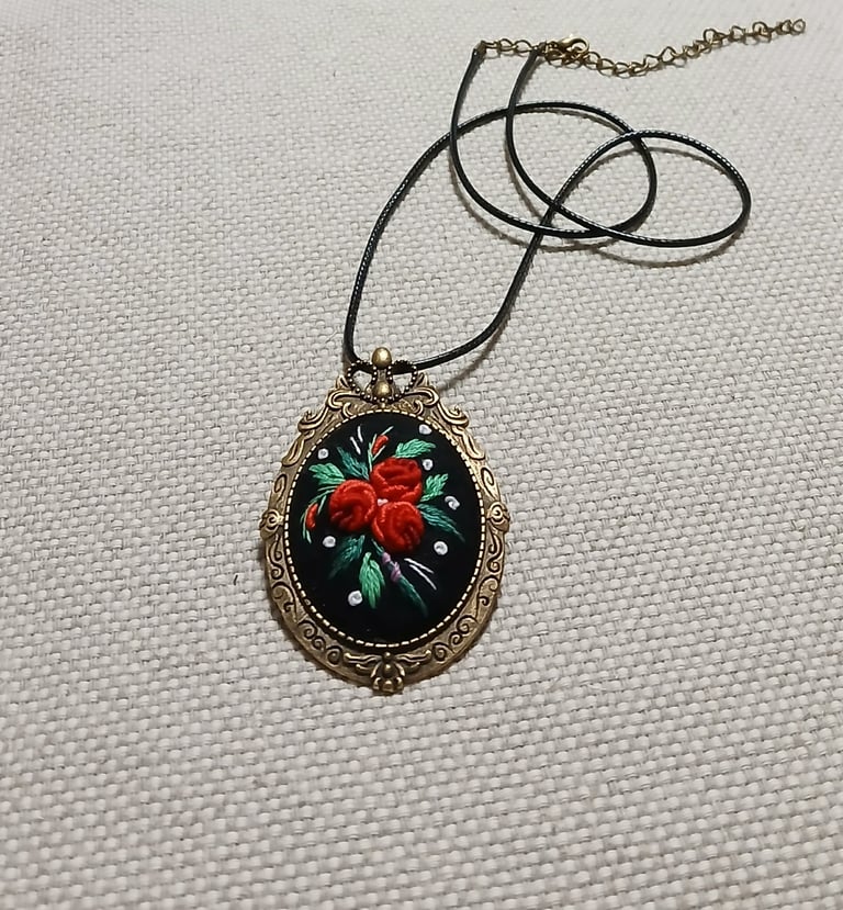 Ornate vintage pendant necklace with red floral design on black background, hanging from thin black cord