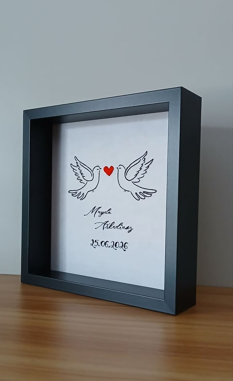 Framed artwork with two doves and a red heart between them, personalized with names and date 25.06.2026 on white background in dark blue frame