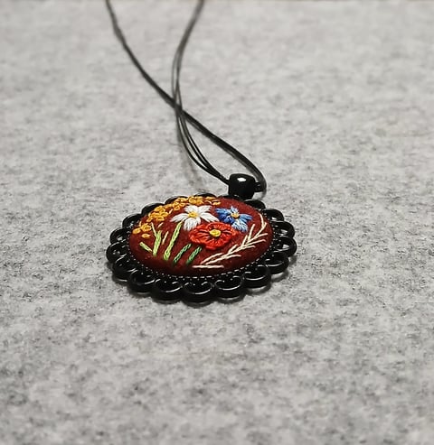 Decorative pendant with red floral design and black scalloped border on gray surface with black cord