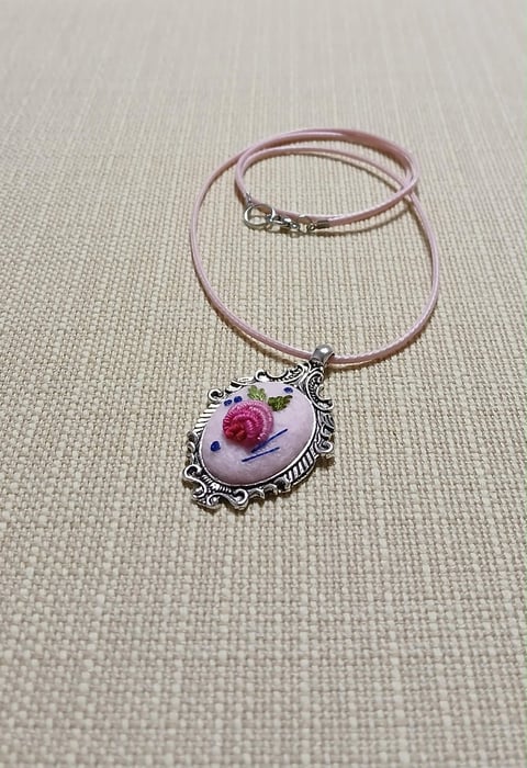 Pink leather cord bracelet with ornate silver pendant featuring a floral rose design on beige textile background