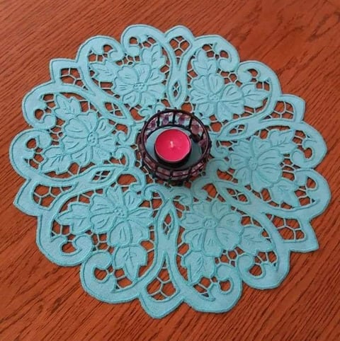 Light blue decorative lace doily with pink candle holder in center on wooden surface