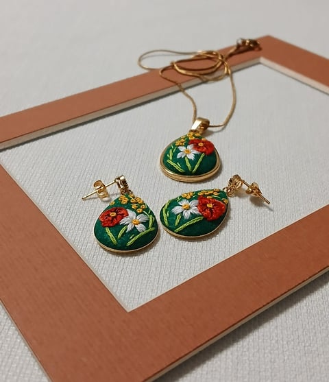 Gold jewelry set with enameled green, red and white floral medallions displayed on tan and white card with matching necklace