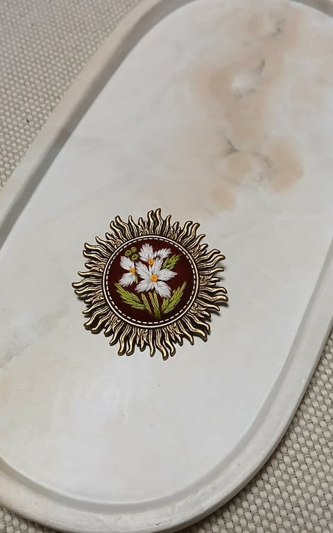 Decorative ceramic plate with ornate botanical illustration of white flowers and green leaves in circular frame with radiating spiky border