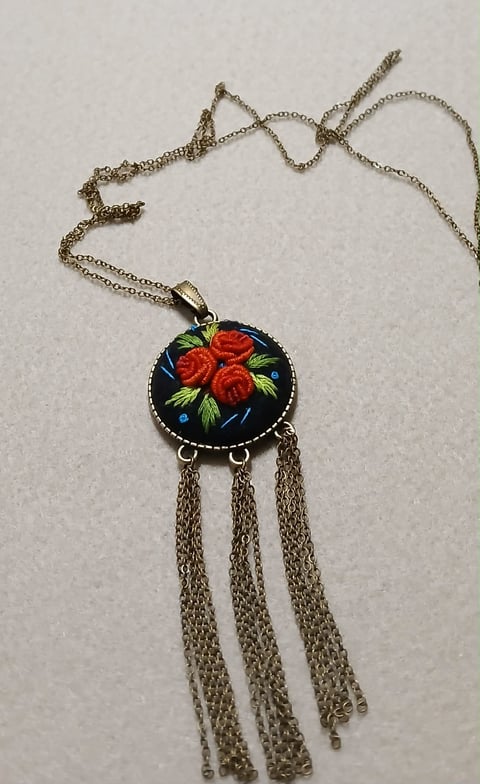 Silver chain necklace with circular pendant featuring red roses on dark background and three dangling chain tassels
