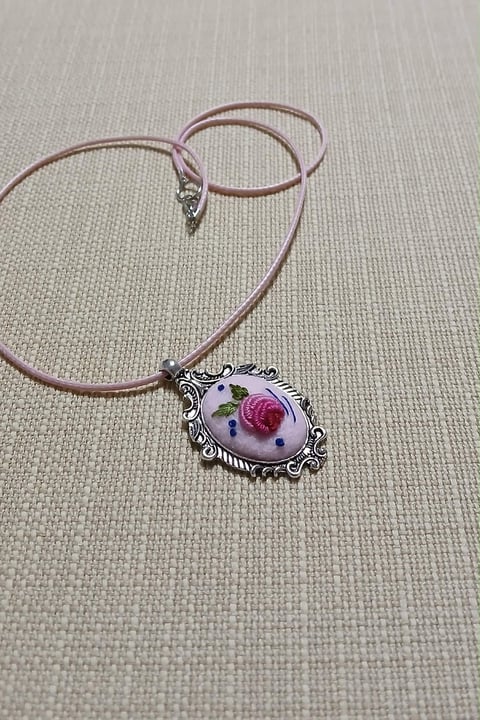 Purple cord necklace with ornate silver pendant featuring a pink rose design on white background
