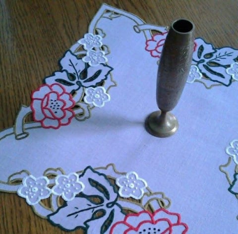 Decorative white fabric napkins with colorful embroidered flowers next to a metal napkin ring on wooden surface