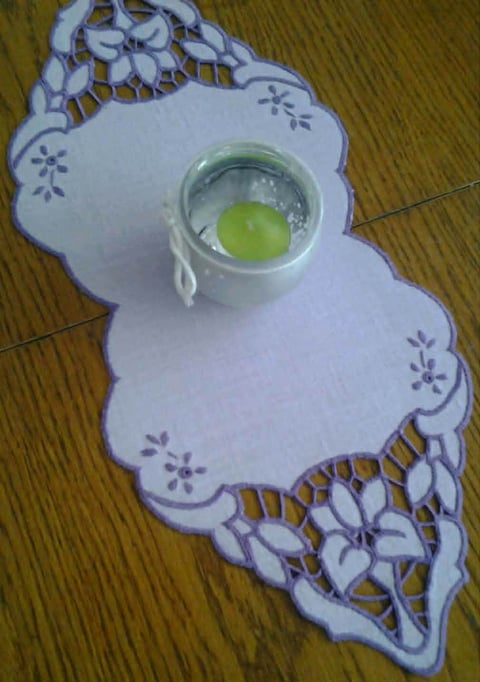 Decorative white lace doily with small glass bowl containing green liquid in center on wooden surface